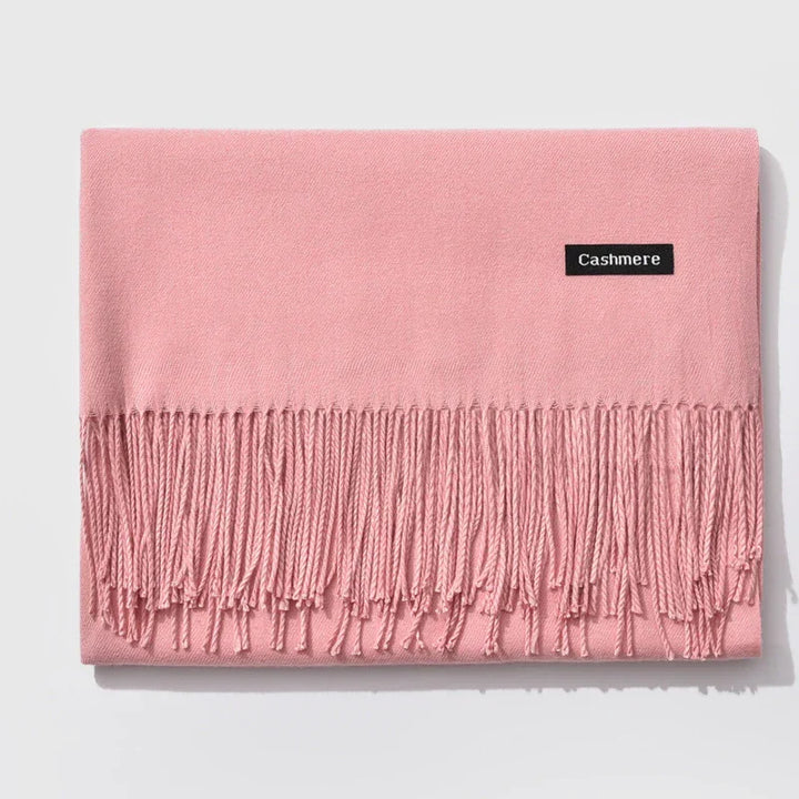 Soft pink cashmere scarf with fringed ends neatly folded on white background