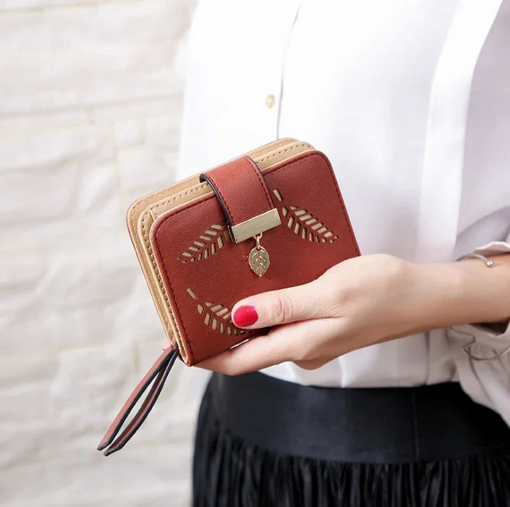 Woman holding small brown leather wallet with leaf cutout design and gold leaf charm