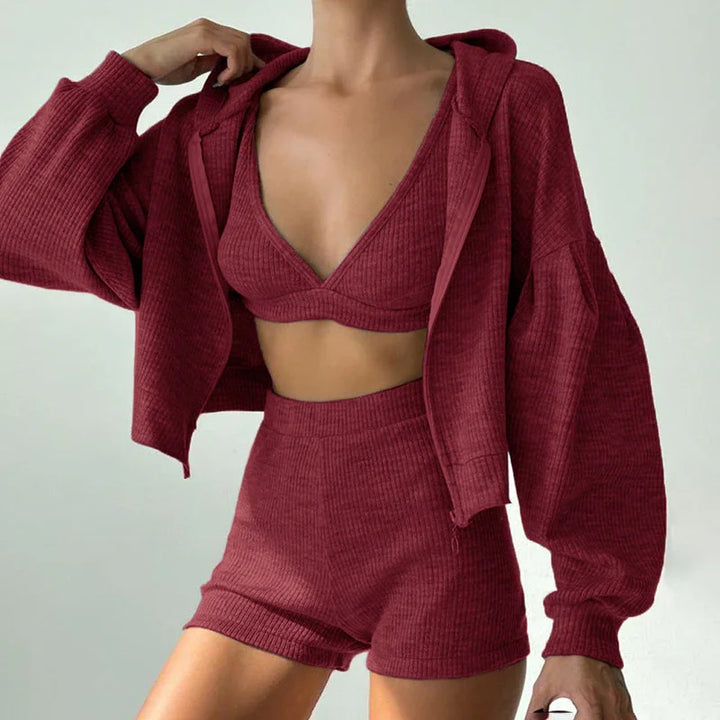 Woman wearing burgundy ribbed knit three-piece lounge set with cropped hoodie, bralette, and shorts