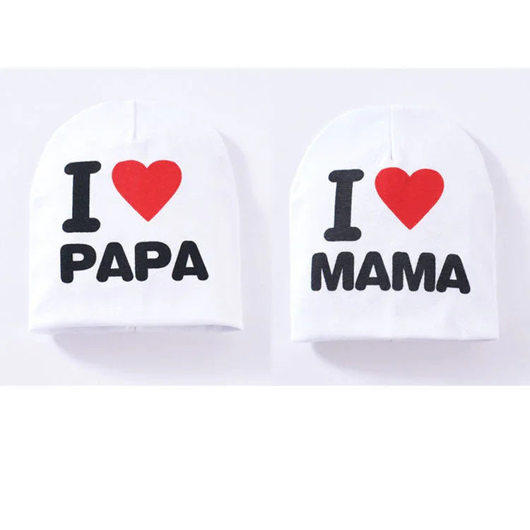 Two white baby hats with black text and red heart reading I love Papa and I love Mama