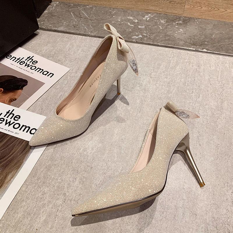 Elegant beige high heel shoes with rhinestone bow detail on tiled floor beside fashion magazines