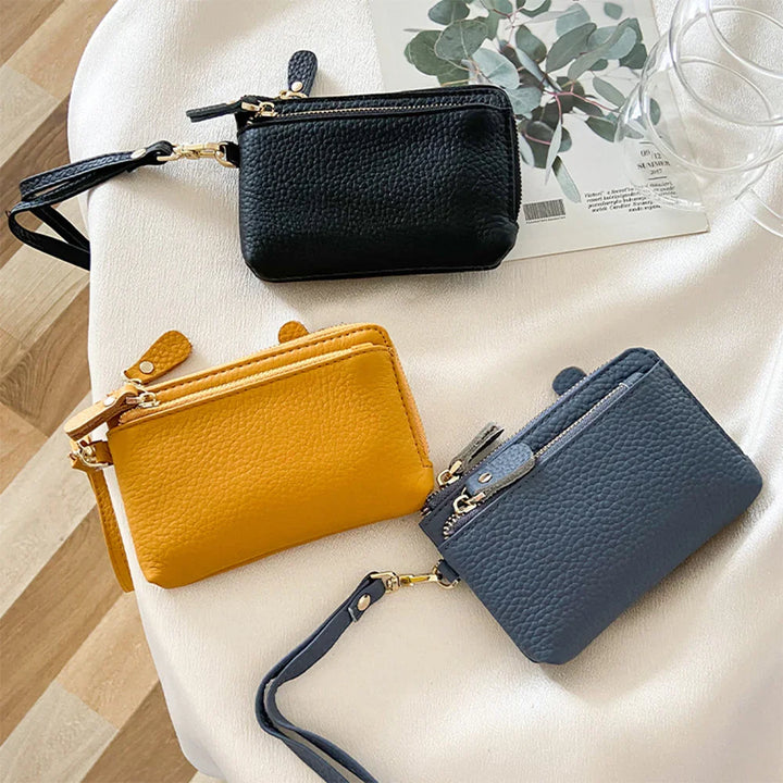Three small textured leather wristlet wallets in black, mustard yellow, and navy on white surface