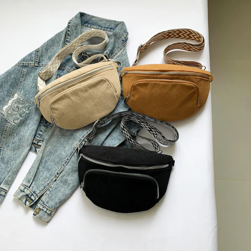 Three corduroy fanny packs in beige, brown, and black with patterned adjustable straps on denim jacket and white surface
