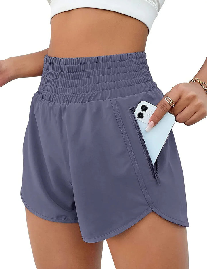 Woman wearing high-waist gray athletic shorts with side zipper pocket holding white smartphone
