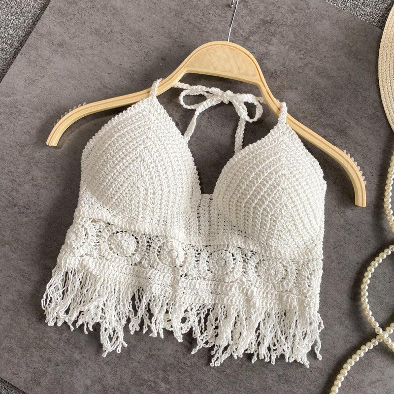 White crocheted halter crop top with fringed hem on wooden hanger against gray fabric