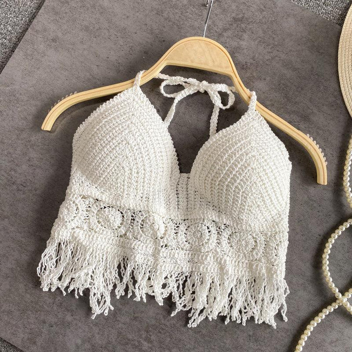White crocheted halter crop top with fringed hem on wooden hanger against gray fabric