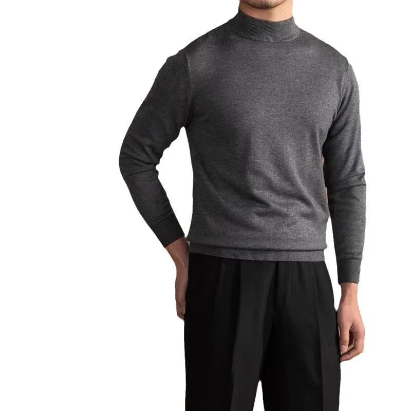 Man wearing a dark gray long sleeve mock neck sweater and black pants against a white background