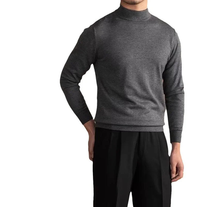 Man wearing a dark gray long sleeve mock neck sweater and black pants against a white background