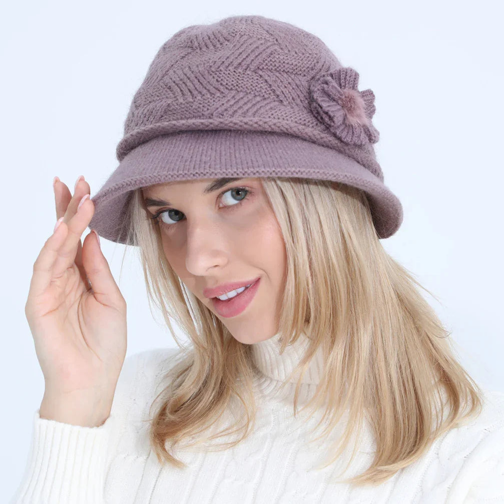 Blonde woman wearing a mauve knitted hat with flower detail and white cable knit sweater