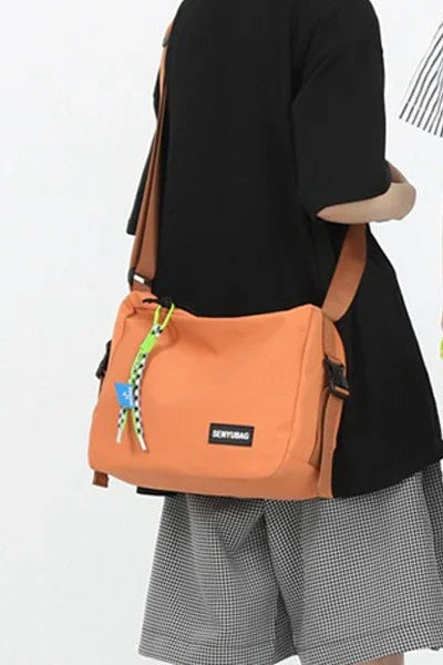 Person wearing orange crossbody bag with SEVYBAG label, dressed in black top and checkered shorts