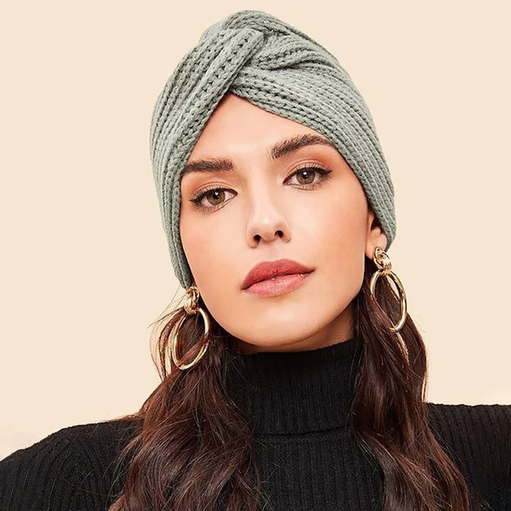 Woman wearing gray knitted turban headband, gold hoop earrings, and black turtleneck sweater