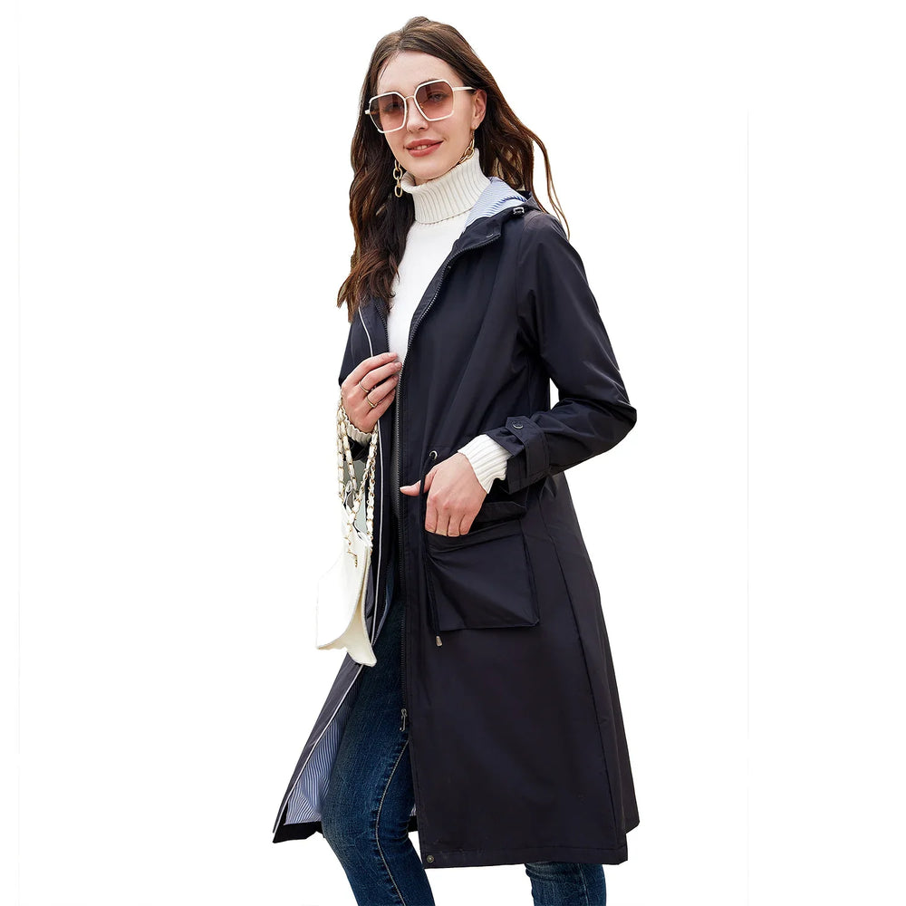 Woman wearing a black long raincoat, white turtleneck sweater, jeans, sunglasses, and carrying a white handbag
