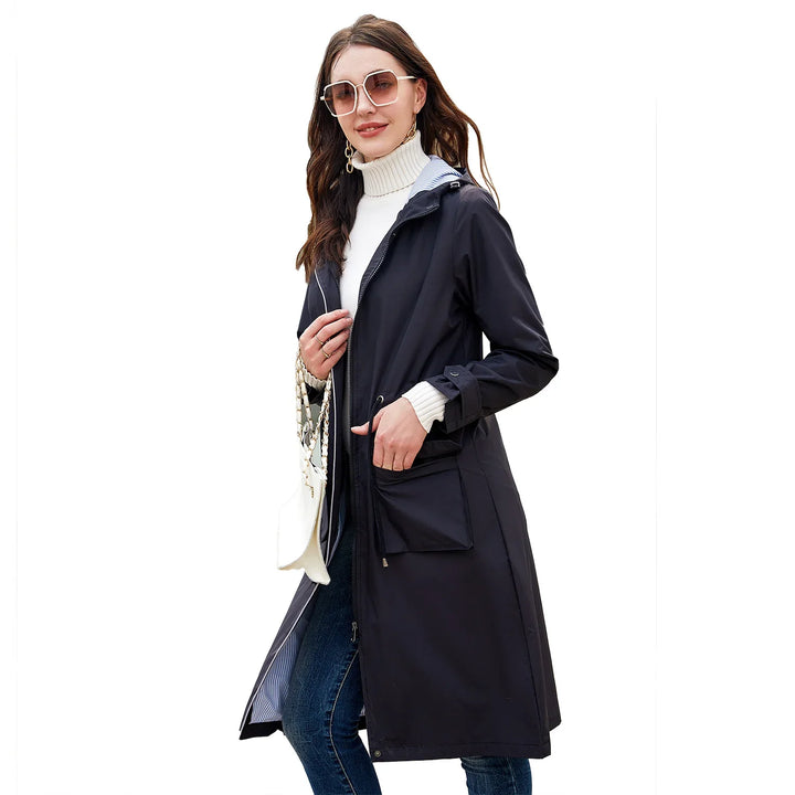 Woman wearing a black long raincoat, white turtleneck sweater, jeans, sunglasses, and carrying a white handbag