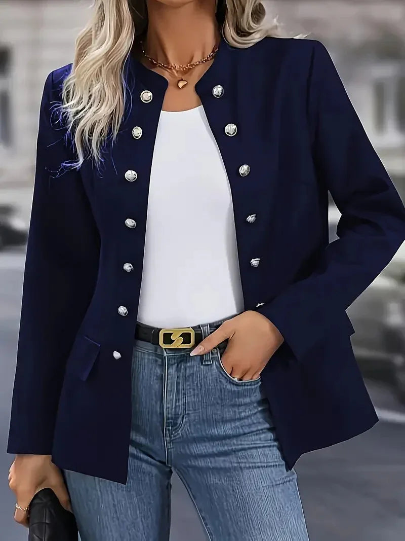 Woman wearing navy blue blazer with silver buttons, white top, blue jeans, and black belt with gold buckle