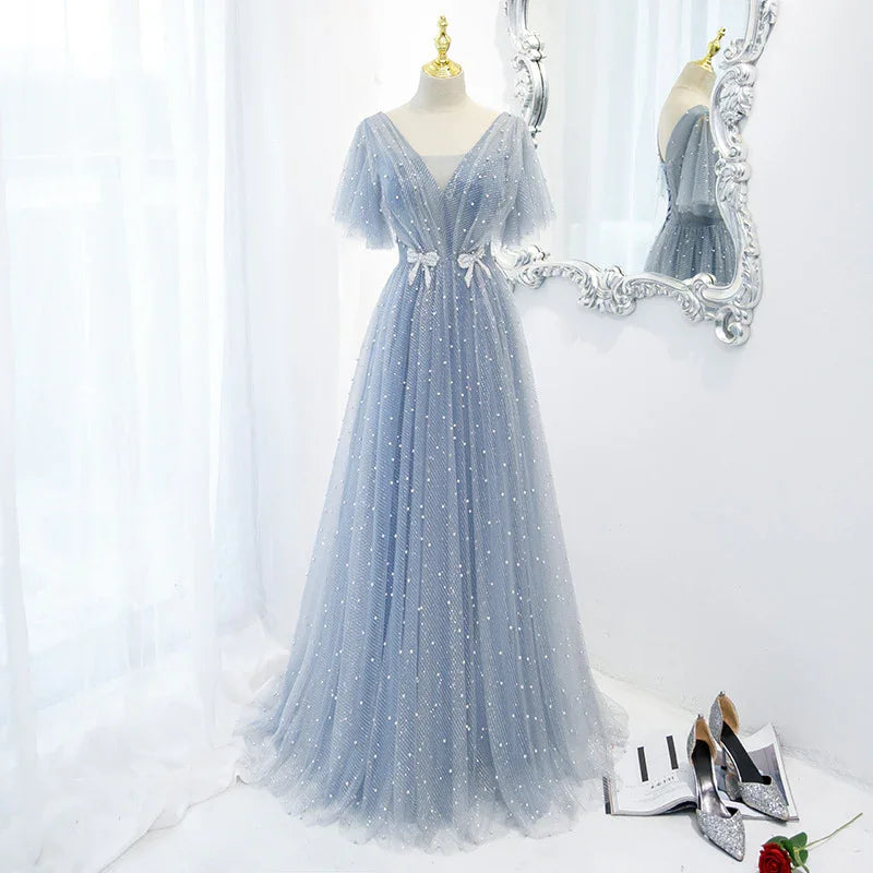 Elegant light blue tulle evening gown with pearl embellishments on mannequin near ornate mirror and silver high heels