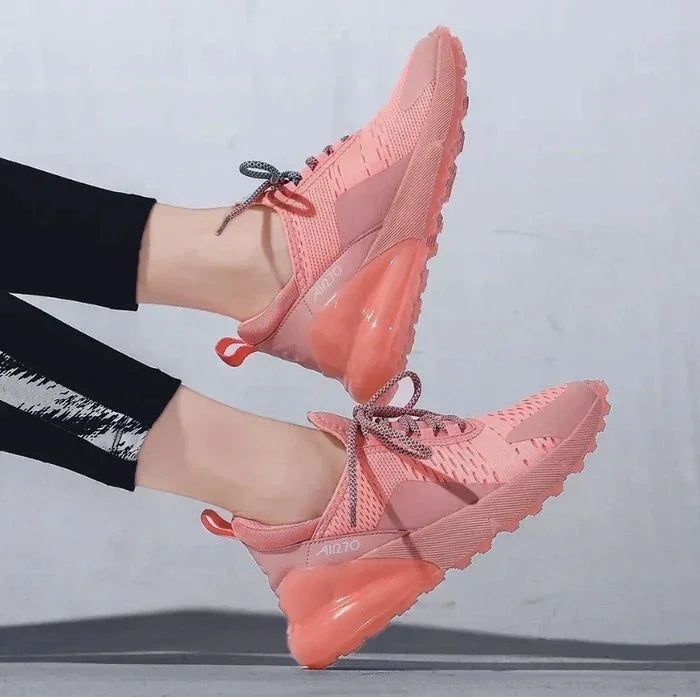 Pair of pink Nike Air Max 270 sneakers with grey laces worn with black leggings on gray surface
