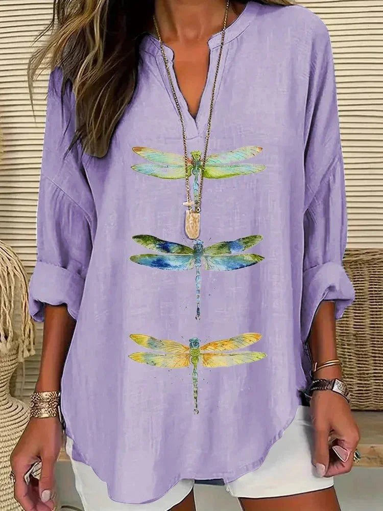 Woman wearing a lavender blouse with colorful dragonfly prints, paired with white shorts and layered necklaces