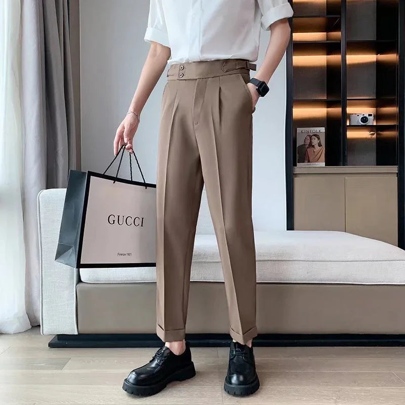 Person wearing beige tailored pants and black shoes holding a Gucci shopping bag in modern living room
