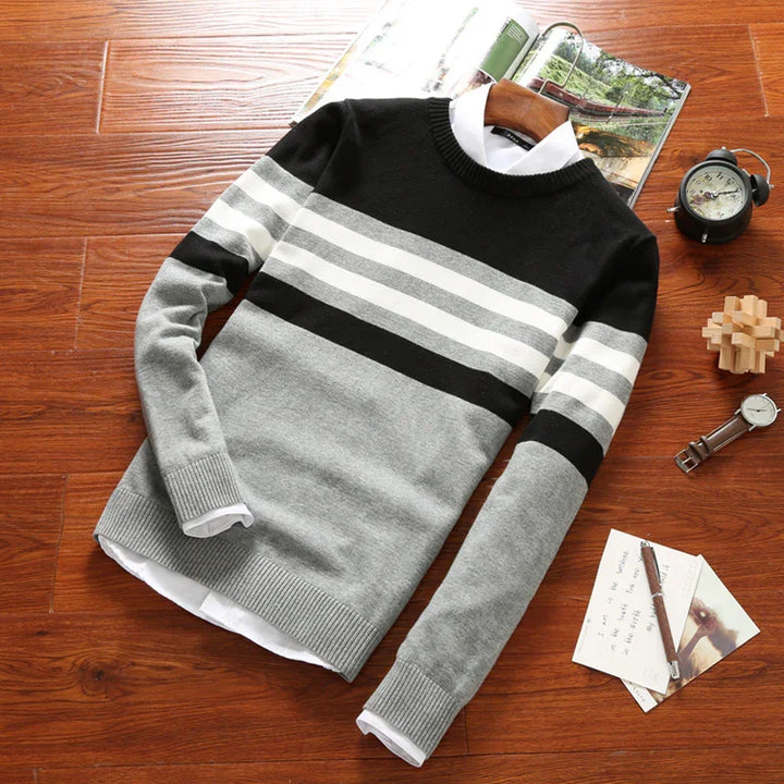 Men's striped knit sweater in black, white, and gray on wooden surface with watch, clock, book, and notes