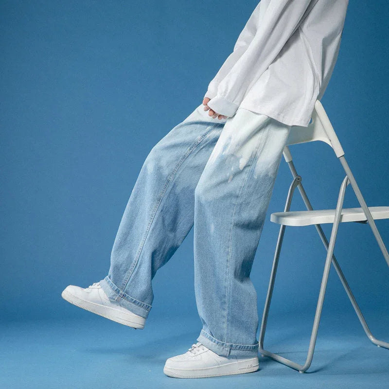 Person wearing white sneakers and baggy light blue bleached jeans sitting on white folding chair against blue background