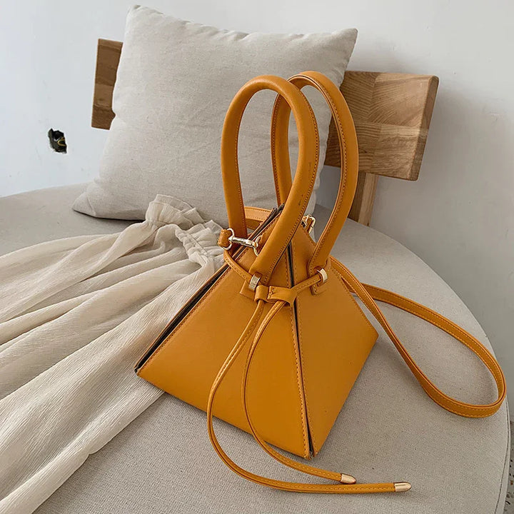 Stylish mustard yellow leather pyramid handbag with double handles on beige fabric chair