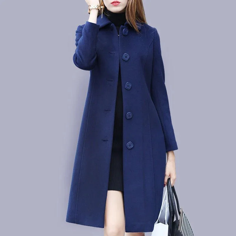 Woman wearing a navy blue wool long coat with large buttons, holding bags, against a gray background