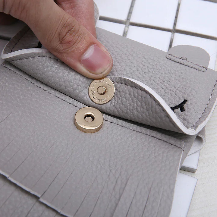 Close-up of hand opening gray leather key holder with gold snap button on white tiled surface