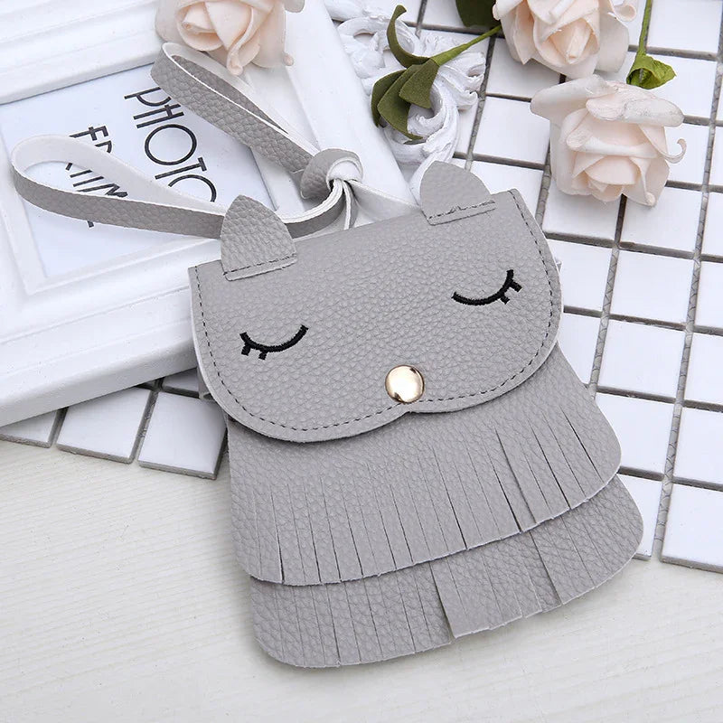 Grey leather wristlet wrist bag with cat ears, embroidered closed eyes, and fringed detailing on white tiled background