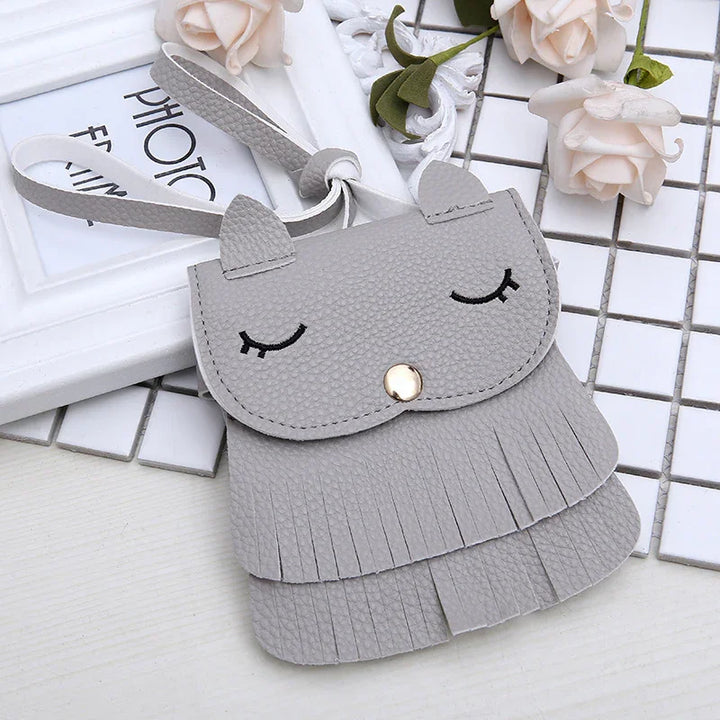 Grey leather wristlet wrist bag with cat ears, embroidered closed eyes, and fringed detailing on white tiled background