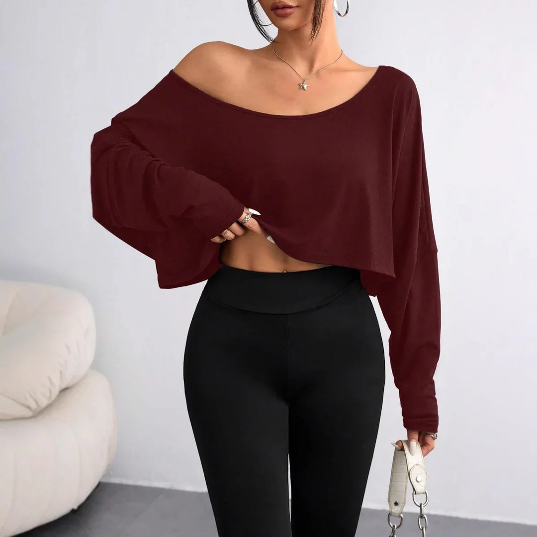 Woman wearing a maroon off-shoulder cropped sweater and high-waisted black leggings indoors