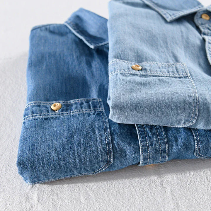 Two folded denim shirts in light and dark blue with wooden buttons on white surface