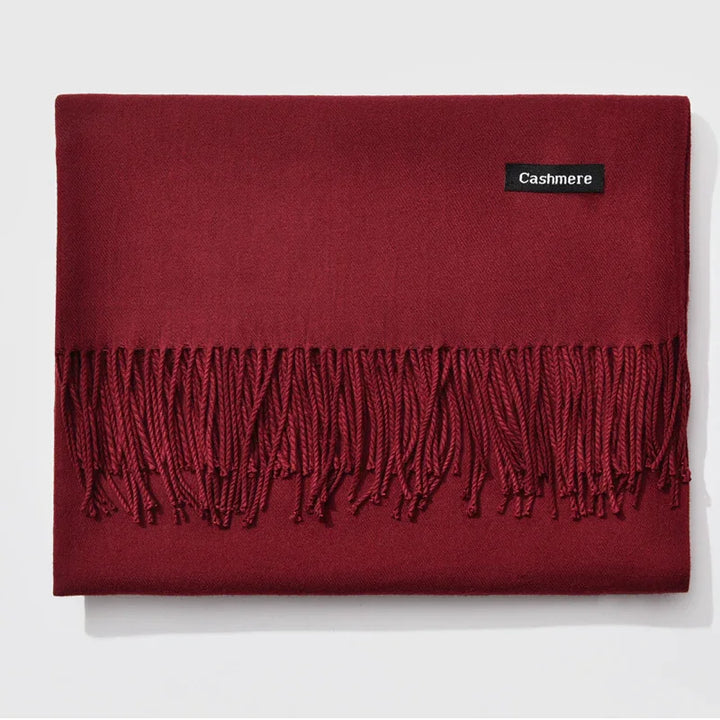 Folded burgundy cashmere scarf with fringe and black label on white background