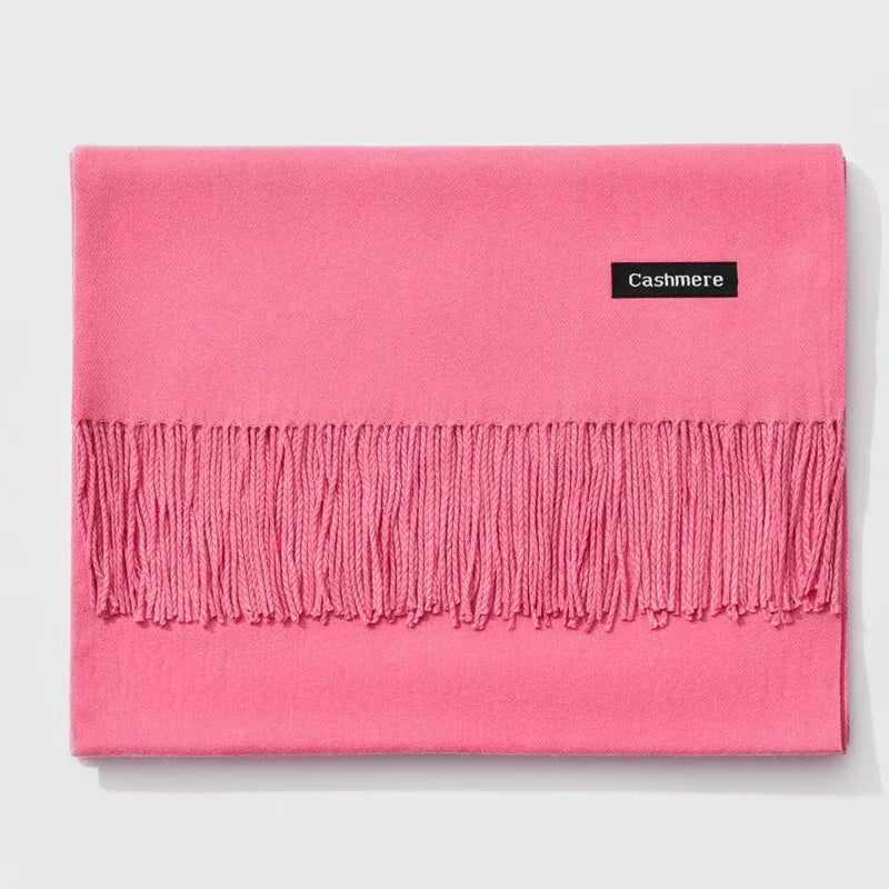 Folded pink cashmere scarf with fringe and black label on light background