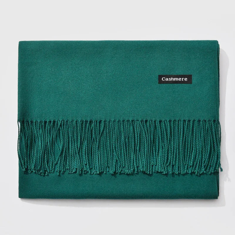 Folded teal green cashmere scarf with fringed edges and black label on white background