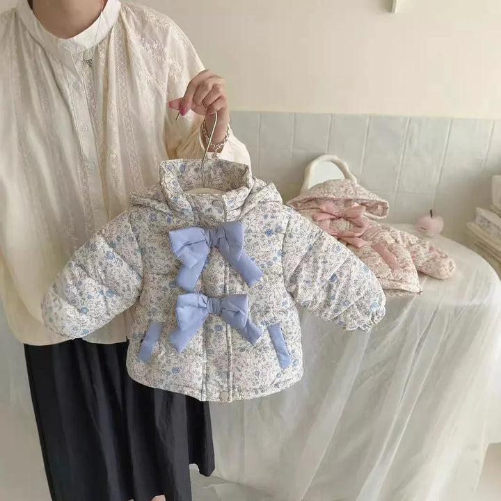 Person holding a floral baby jacket with blue bows, beige padded fabric, and a hood