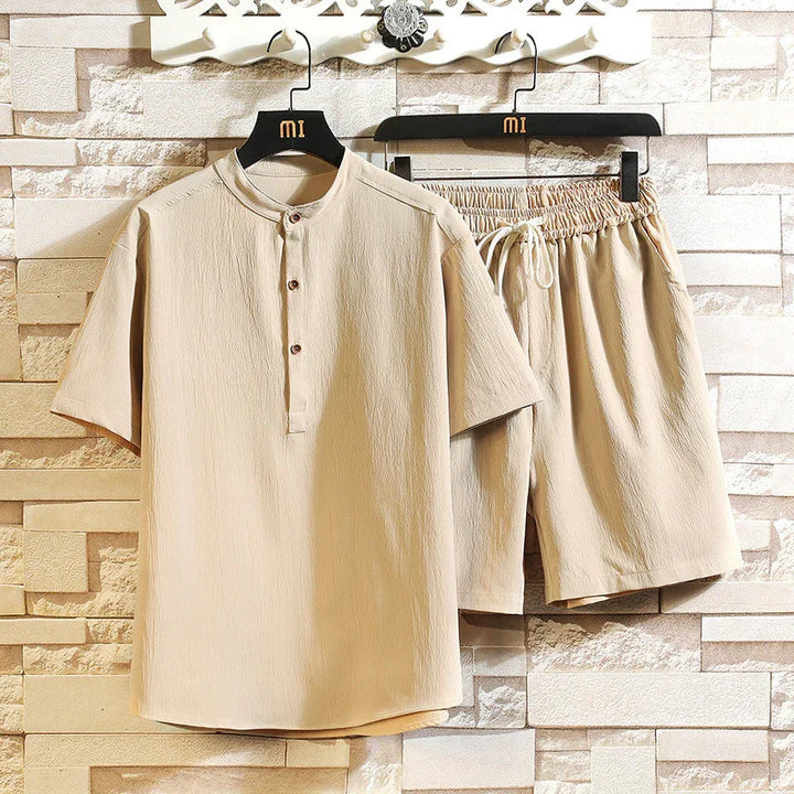 Beige casual men's short sleeve shirt and elastic waist shorts set hanging on black hangers against stone wall