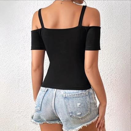 Woman wearing black off-shoulder top with straps and distressed light blue denim shorts against white textured wall
