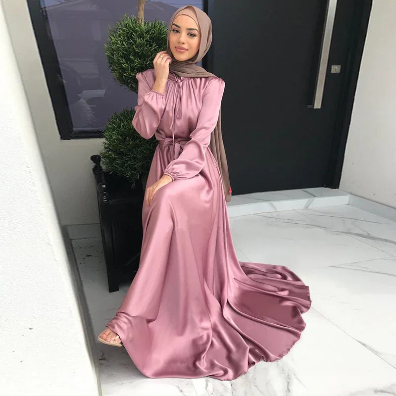 Woman wearing a satin mauve maxi dress and brown hijab seated indoors on white marble floor