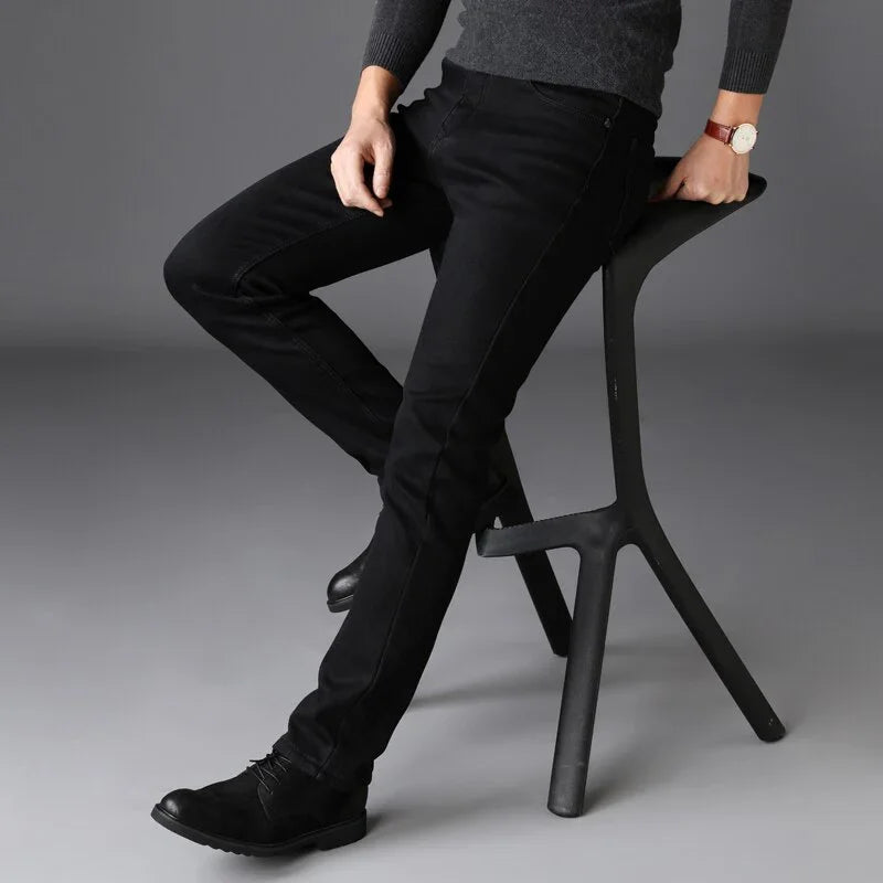 Man wearing black slim-fit jeans and black boots sitting on a modern black stool