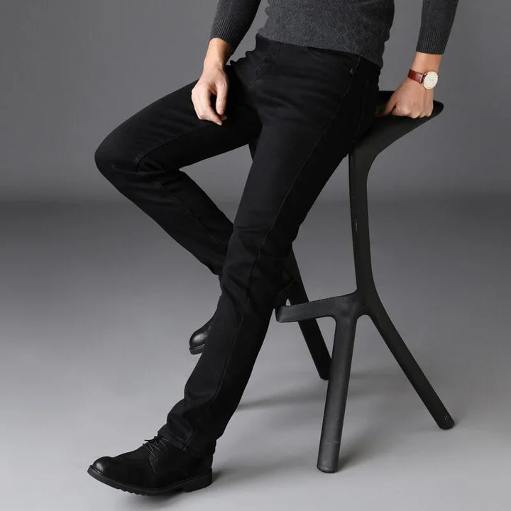 Man wearing black slim-fit jeans and black boots sitting on a modern black stool