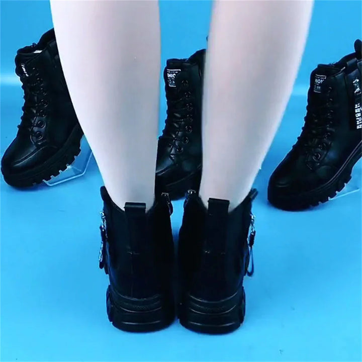 Person wearing black leather combat boots on blue floor with two similar boots nearby