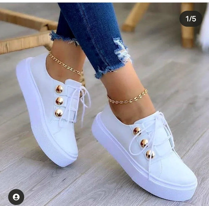 White platform sneakers with gold button accents worn with ripped blue skinny jeans and gold ankle bracelets on wood floor