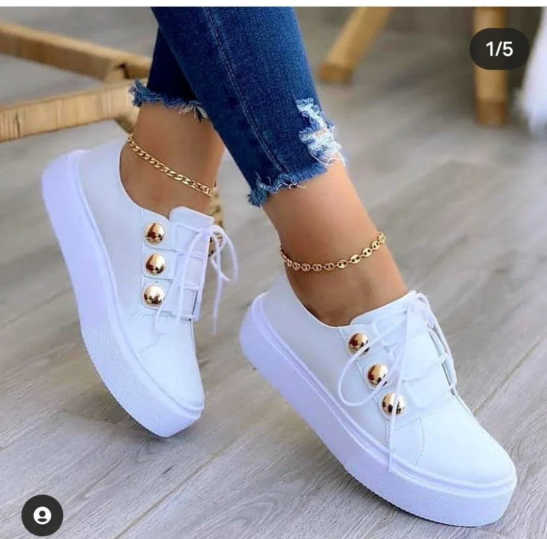 White platform sneakers with gold buttons worn with ripped blue jeans and gold anklets on wooden floor