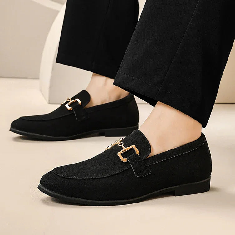 Black suede men's loafers with gold buckle detail paired with black dress pants