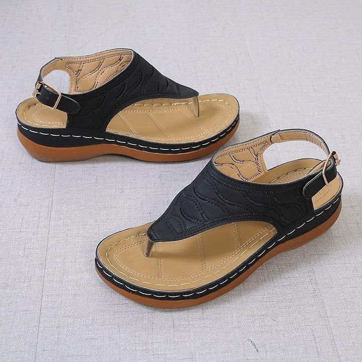 Pair of black leather sandals with cushioned tan insoles and brown rubber soles on gray surface