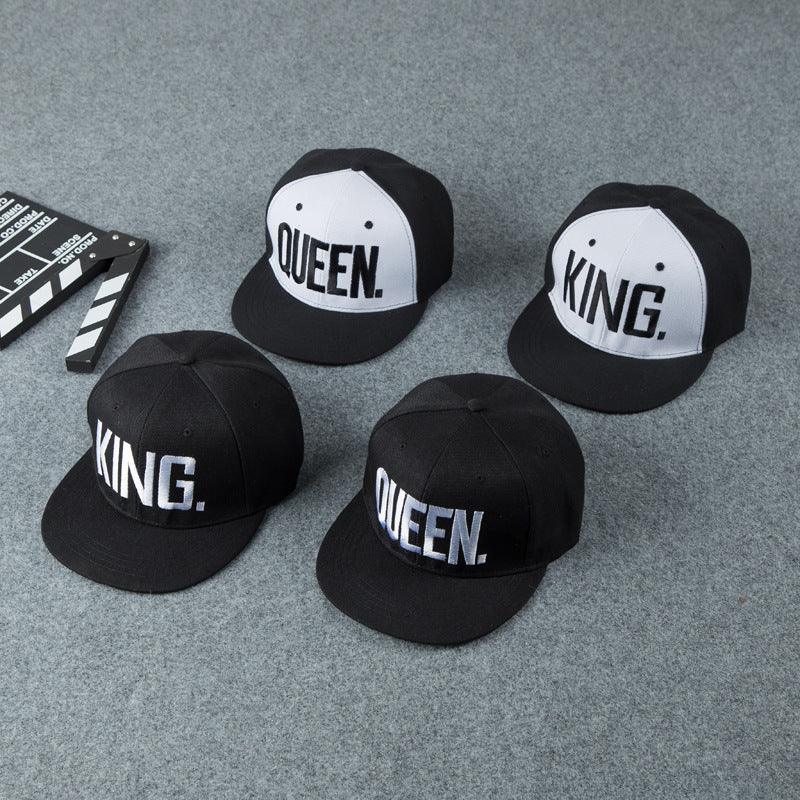 Four black and white snapback caps on gray carpet, two with KING. and two with QUEEN. text