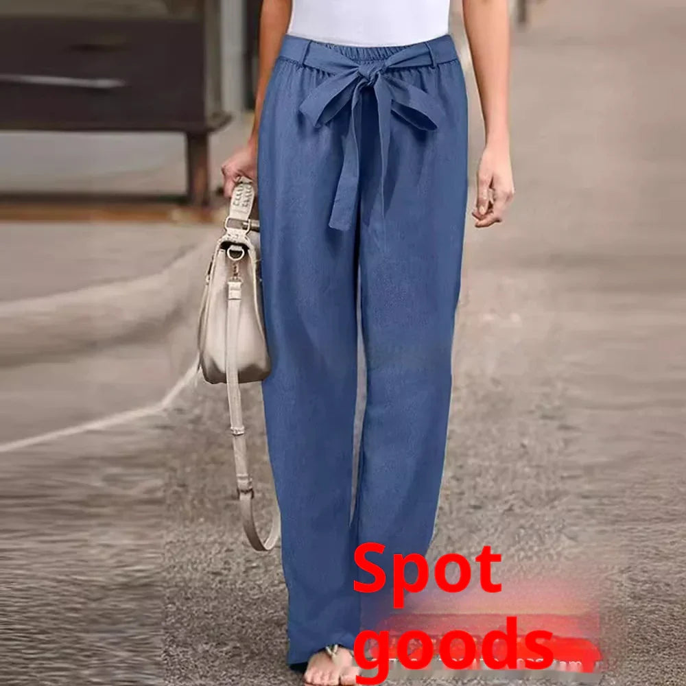Woman wearing blue paperbag waist pants with a tied bow and holding a beige handbag