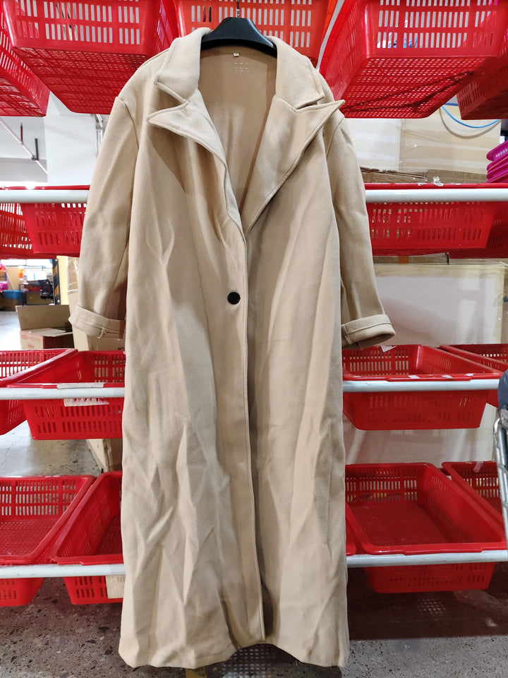 Beige long coat with lapel collar and black button hanging on a rack in a warehouse with red plastic baskets