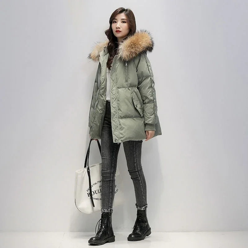 Woman wearing green puffer jacket with fur hood, grey skinny jeans, black boots, and carrying white tote bag