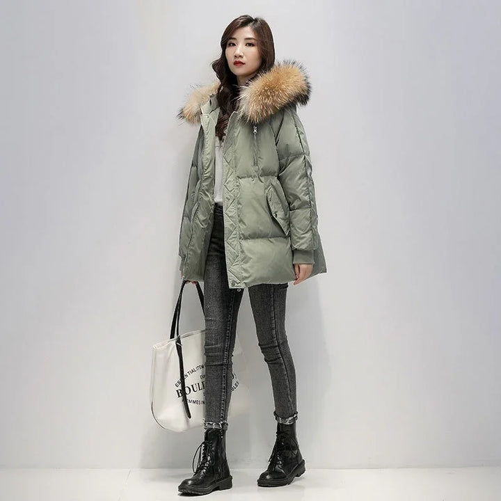 Woman wearing green puffer jacket with fur hood, grey skinny jeans, black boots, and carrying white tote bag